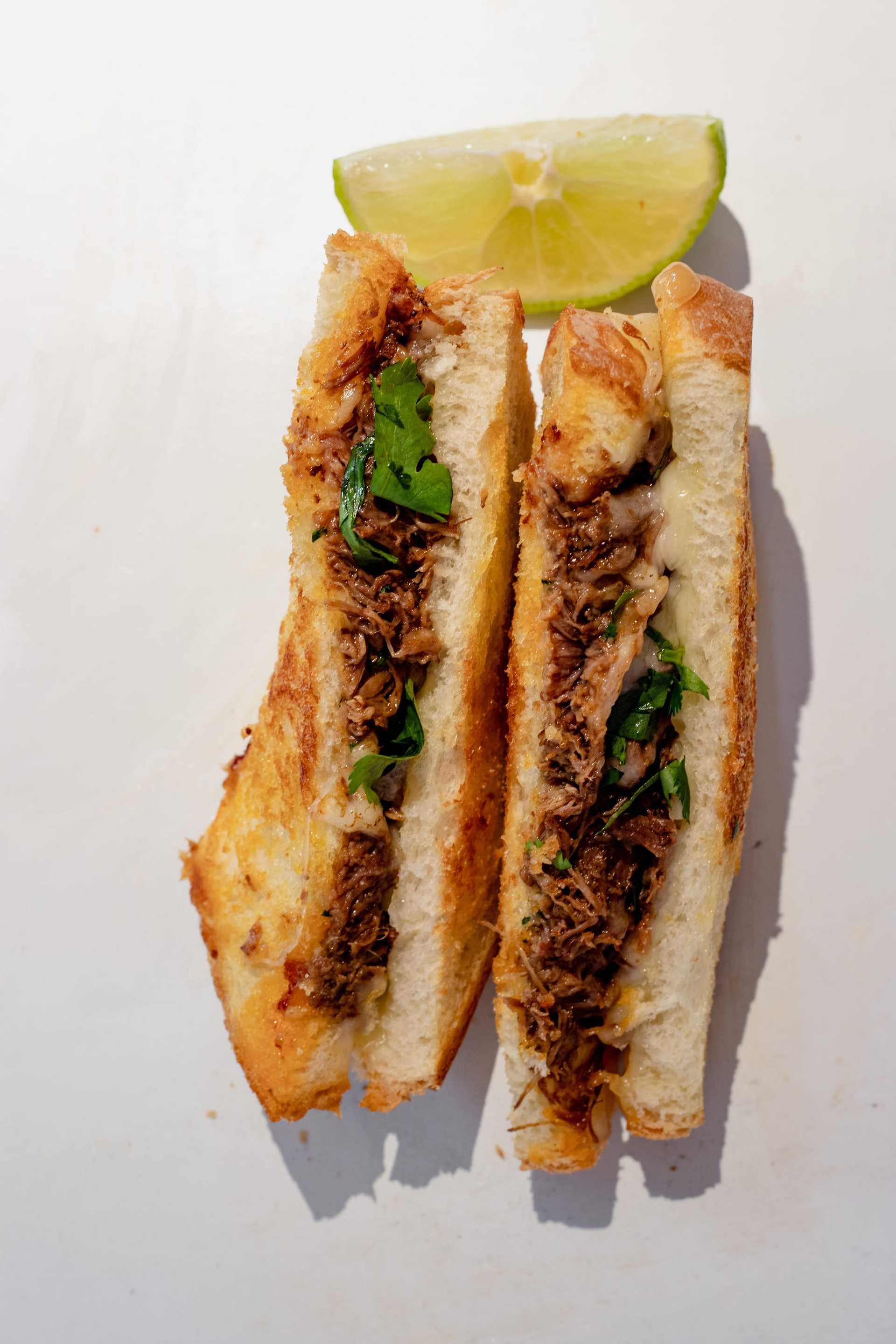 Grilled sandwich with shredded meat, cilantro, and melted cheese, served with a lime wedge.