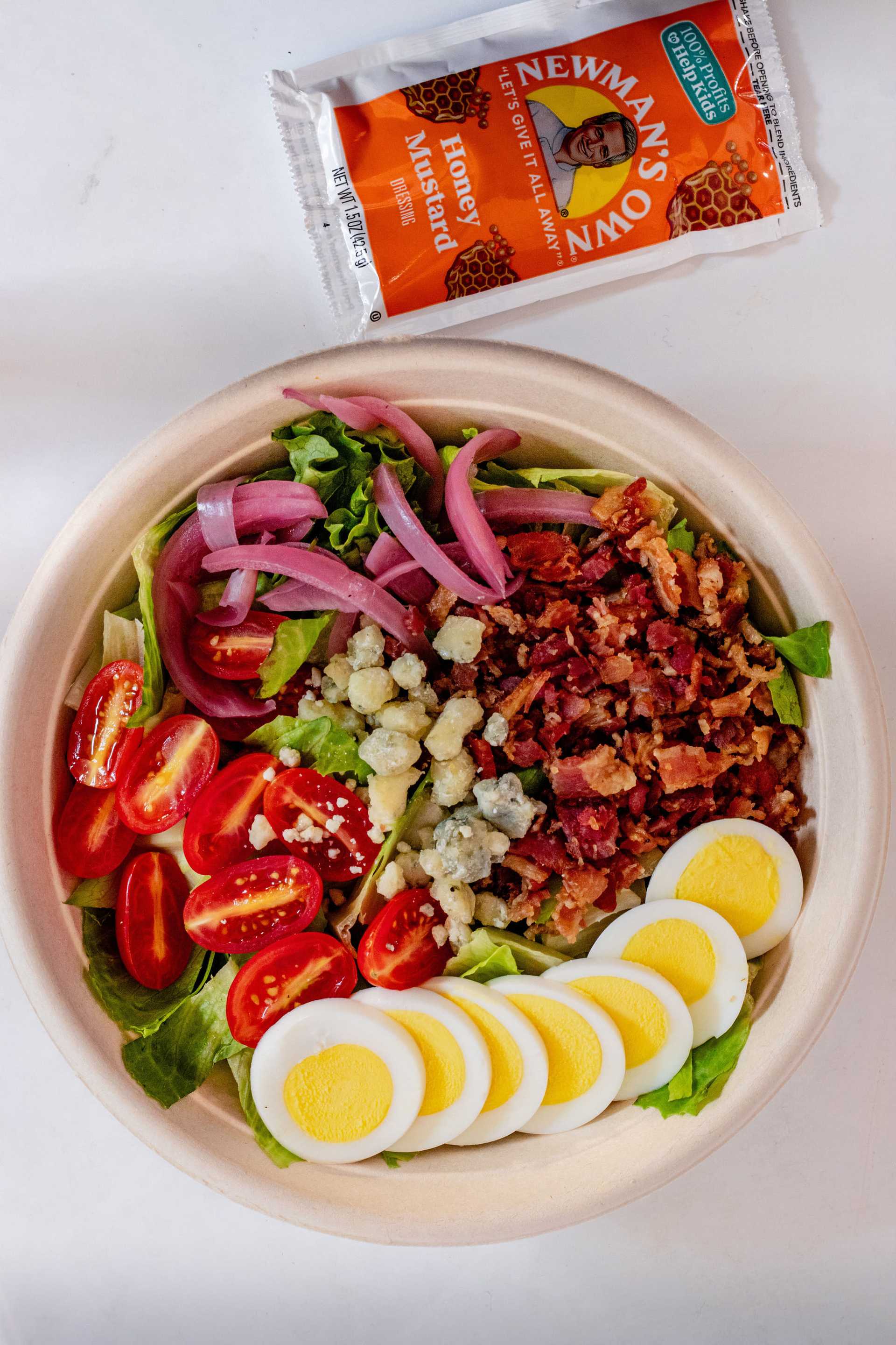 Salad with boiled eggs, cherry tomatoes, bacon, blue cheese, onions, and honey mustard dressing.