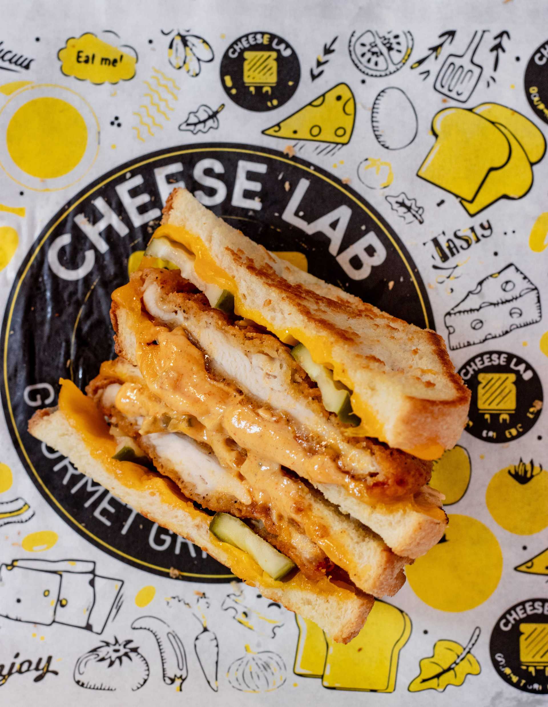 Grilled cheese sandwich with chicken and sauce on branded paper.